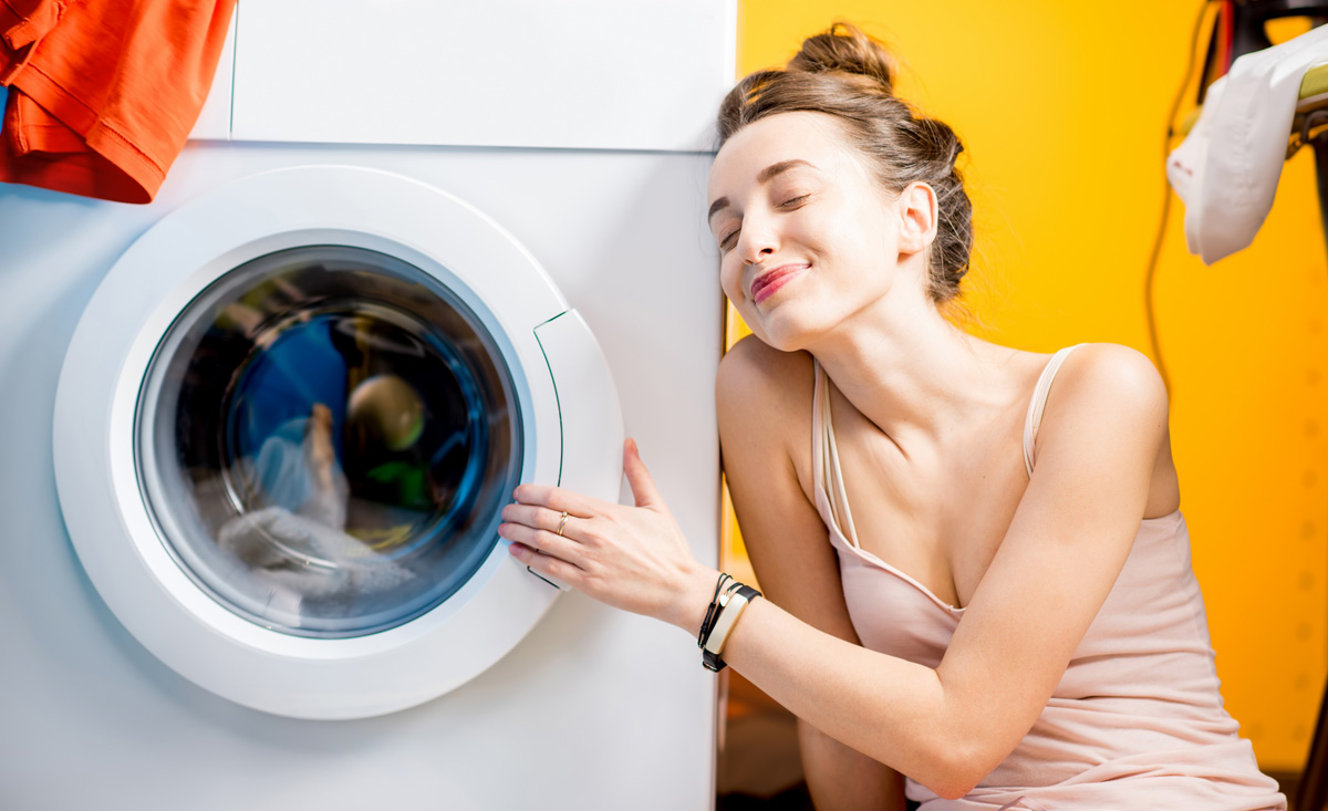 Жена в купальнике забрасывает одежду в стиралку фото